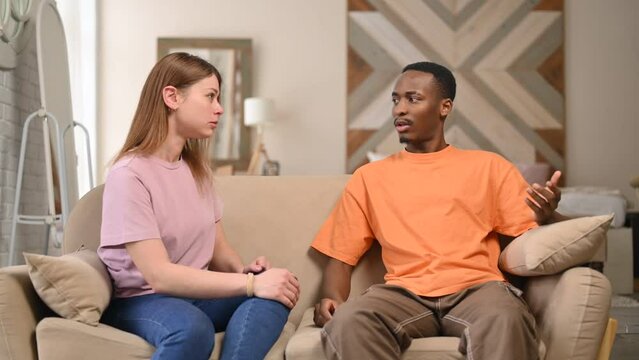 Young people arguing on the sofa at home. A young woman scolds and humiliates her partner, who can only make excuses and listen to dissatisfaction