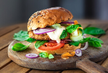 Grilled burger with vegetarian cutlet and vegetables on a wooden board