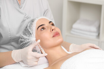 Professional cosmetologist holding skincare ampoule while working with client in clinic, closeup
