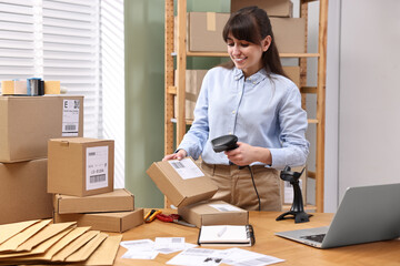 Parcel packing. Post office worker with scanner reading barcode at wooden table indoors