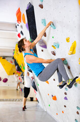 Confident female mountaineer climbing artificial rock wall without belay indoors