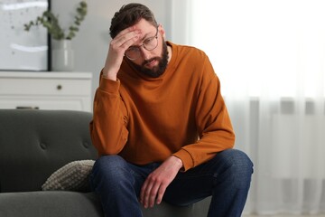 Overwhelmed man in glasses sitting on sofa at home