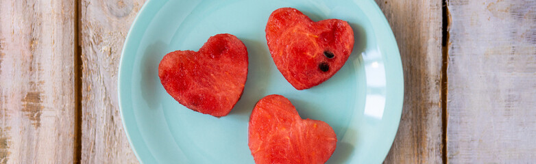 Summer flat lay. Watermelon hearts on a blue plate on wooden background. Sun glasses, shells, sea...