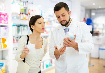 Obraz premium Young adult man pharmacist consulting woman customer about products at pharmacy