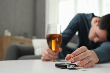 Drunk man reaching for car keys indoors, selective focus. Space for text