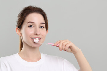Smiling woman with dental braces cleaning teeth on grey background. Space for text