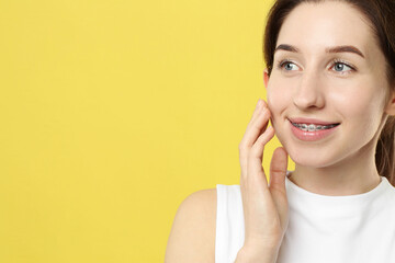 Portrait of smiling woman with dental braces on yellow background. Space for text