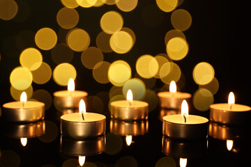 Burning candles on mirror surface in darkness, bokeh effect