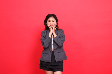 gesture of an Asian office woman pouting with both hands holding her cheeks wearing a gray jacket...
