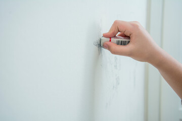 An unrecognizable hand erases pencil marks on the wall with an eraser