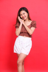 Portrait of a cheerful Asian woman posing for sleep wearing a brown blouse and shorts on a red...