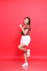 full body cheerful Asian woman model poses in a relaxed dance wearing a brown blouse and shorts on...