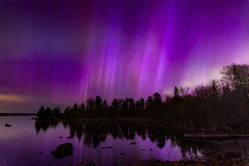 Northern lights erupt over a lake in Minnesota in a dark sky overhead shining rainbow of Aurora light
