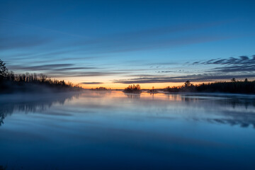 Dawn on a northern Minnesota lake near Duluth brings bright colors to the sky as steam rises from...