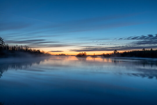 Dawn on a northern Minnesota lake near Duluth brings bright colors to the sky as steam rises from the water creating a gentle fog