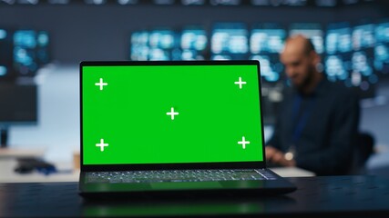 Focus on green screen laptop in server room used by man in blurry background to safeguard data from...