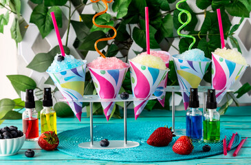 Colourful snow cones with crazy straws and flavoured syrups in front.