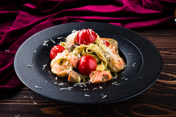 A black plate with shrimp, tomatoes, and pasta  delicious food presentation
