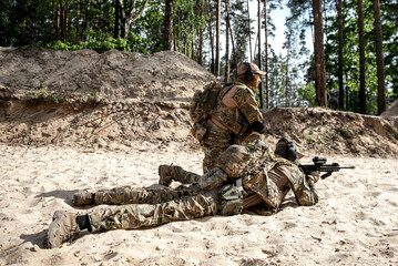Soldiers in camouflage lies on the sand and shoots