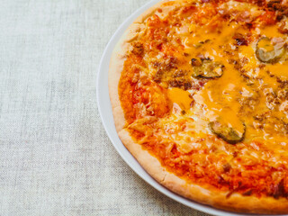 Cooked burger style Italian pizza with tomato sauce, meat, cucumber and cheese on round metal tray and light color table cloth. Ready meals product for cooking home. High quality ingredients