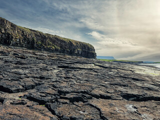 Rough stone coastline with cliff and silhouette of Benbulben flat top mountain in the background....