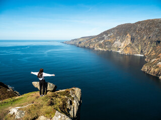 Teenager girl on a trip to Slieve League Cliff, Ireland. Stunning nature scenery with cliff, ocean...
