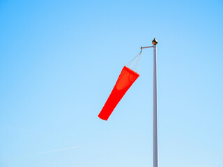 Red windsocks on metal pole indicates weak wind, blue sky background. Safety measure at airport....