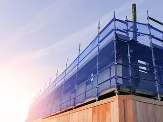 Construction area with ply wood safety fence and scaffolding covered in blue plastic mesh for...