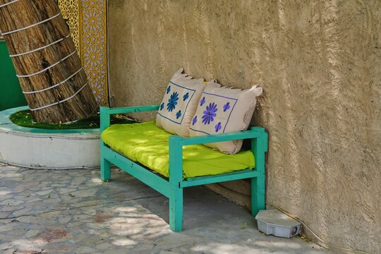 View of traditional painted wooden bench with decorative fabric cushions with classic arabic motif in courtyard villa. 