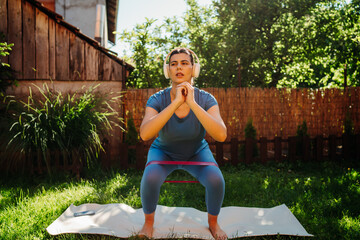 One young caucasian woman is doing exercises with resistance band on yoga mat in her backyard	
