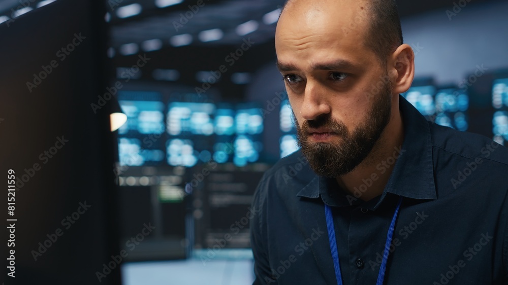Poster overworked engineer feeling stressed while coding in data center facility, trying to ensure optimal 