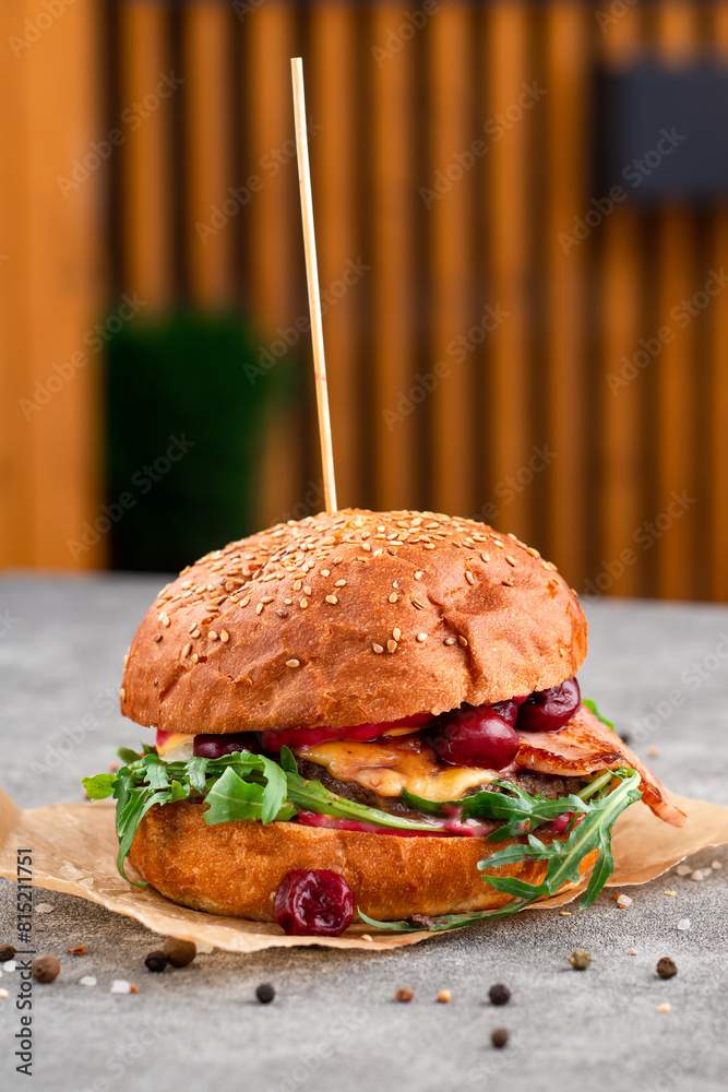 Wall mural creative craft burger with fried slices of bacon and cherry, fresh arugula. street food concept.