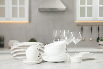Clean plates, bowls, cups and glasses on white marble table in kitchen
