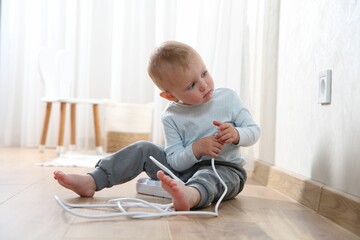 Little child playing with power strip plug near electrical socket at home. Dangerous situation