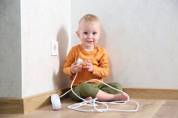 Little child playing with power strip plug near electrical socket at home. Dangerous situation