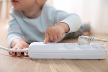 Little child playing with power strip on floor indoors, closeup. Dangerous situation