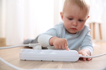 Little child playing with power strip on floor indoors, selective focus. Dangerous situation