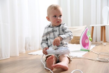 Little child playing with power strip and iron plug on floor at home. Dangerous situation