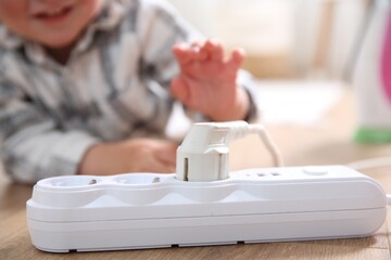 Little child playing with power strip and plug on floor indoors, closeup. Dangerous situation