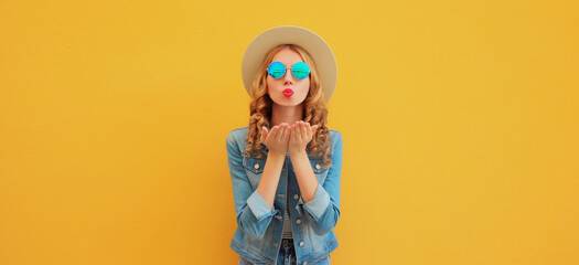 Portrait beautiful stylish young woman blowing kiss in summer hat posing on yellow studio background