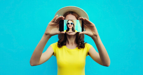 Close up portrait of woman taking selfie with mobile phone stretching her hands on blue background