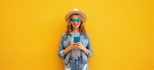 Summer portrait of happy young woman with mobile phone looking at device on yellow background