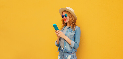 Summer portrait of happy young woman with mobile phone looking at device on yellow background