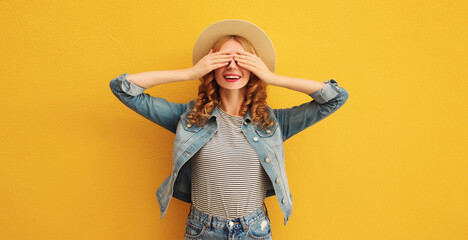 Stylish surprised young woman covering her eyes with hands in summer straw hat on orange background