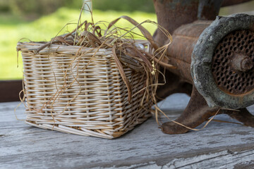  wicker basket filled with dried grass and a rusted metal meat grinder on a wooden table. The white...