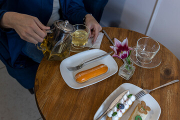 On the wooden table, there's a white plate with an eclair and a cream pastry topped with a...