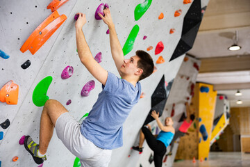 Young man climbing on rock-climbing wall during training in bouldering gym. © JackF