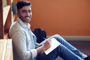 Male student, portrait and smile in library for study in university with notebook for education with writing. Scholarship, academic and research for knowledge on campus for doctorate in London.