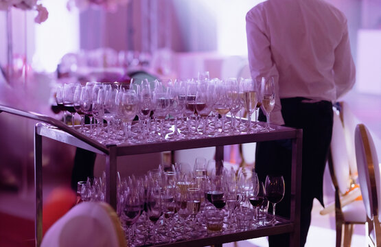 The waiter collects dirty glasses and dishes from the tables after the banquet. Remains of alcohol, wine in glasses after the party.