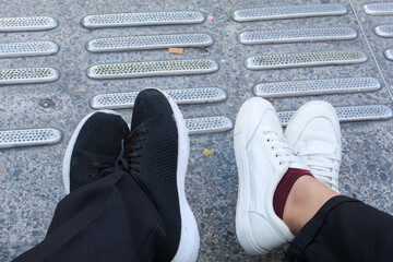 Portrait of two friends wearing black and white shoes on the sidewalk.